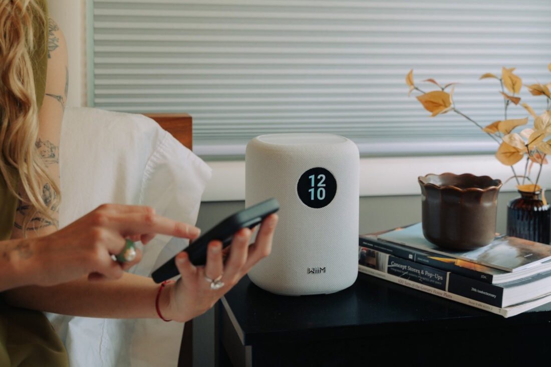 WiiM-Sound-foto-1-scaled Persona con teléfono móvil al lado de altavoz inteligente sobre una mesa