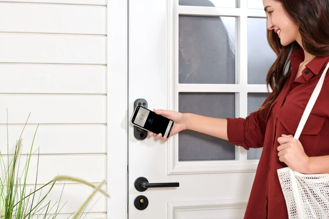 smart-lock-u200-black-04 Mujer acercando el móvil a una cerradura inteligente para abrir la puerta principal